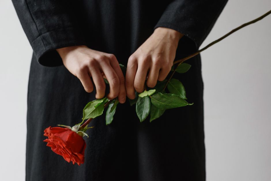 한 사람이 선명한 붉은색 꽃 한 송이를 부드럽게 잡고 있는 모습